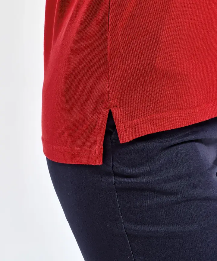 Gros plan sur la fente latérale d'un polo femme rouge au-dessus d'un pantalon marine